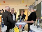 Personen stehen feierlich an einem Stehtisch und unterhalten sich.