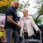 Ein Pfleger begrüßt eine Seniorin beim Aussteigen aus dem Fahrdienst. 