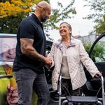 Ein Pfleger begrüßt freundlich eine Seniorin, die aus dem Fahrdienst aussteigt.