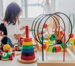 Bunte Spielsachen auf einem Tisch. Im Hintergrund spielt ein Mädchen. 