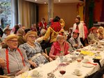 Seniorinnen und Senioren sitzen an einer großen Tafel haben hüte auf und feiern Fasching.