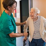Eine Pflegerin hilft einer Seniorin am Gehbock. 