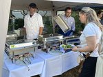 Das Essensbuffet mit dem Küchenpersonal auf der einen Seite und einer Besucherin auf der anderen Seite des Tisches.