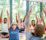 Eine vielfältige Gruppe aus Menschen strecken beim gemeinsamen Yoga die Arme nach oben. 