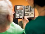 Ein Senior und eine Pflegerin schauen sich gemeinsam ein Fotoalbum an.