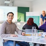 Ein junger Mann sitzt in einem Klassenzimmer am Schreibtisch.