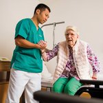 Ein Pfleger hilft einer Seniorin beim Aufstehen. 