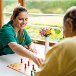 Eine Pflegerin spielt mit einem Senior das Brettspiel Mensch ärgere dich nicht. 